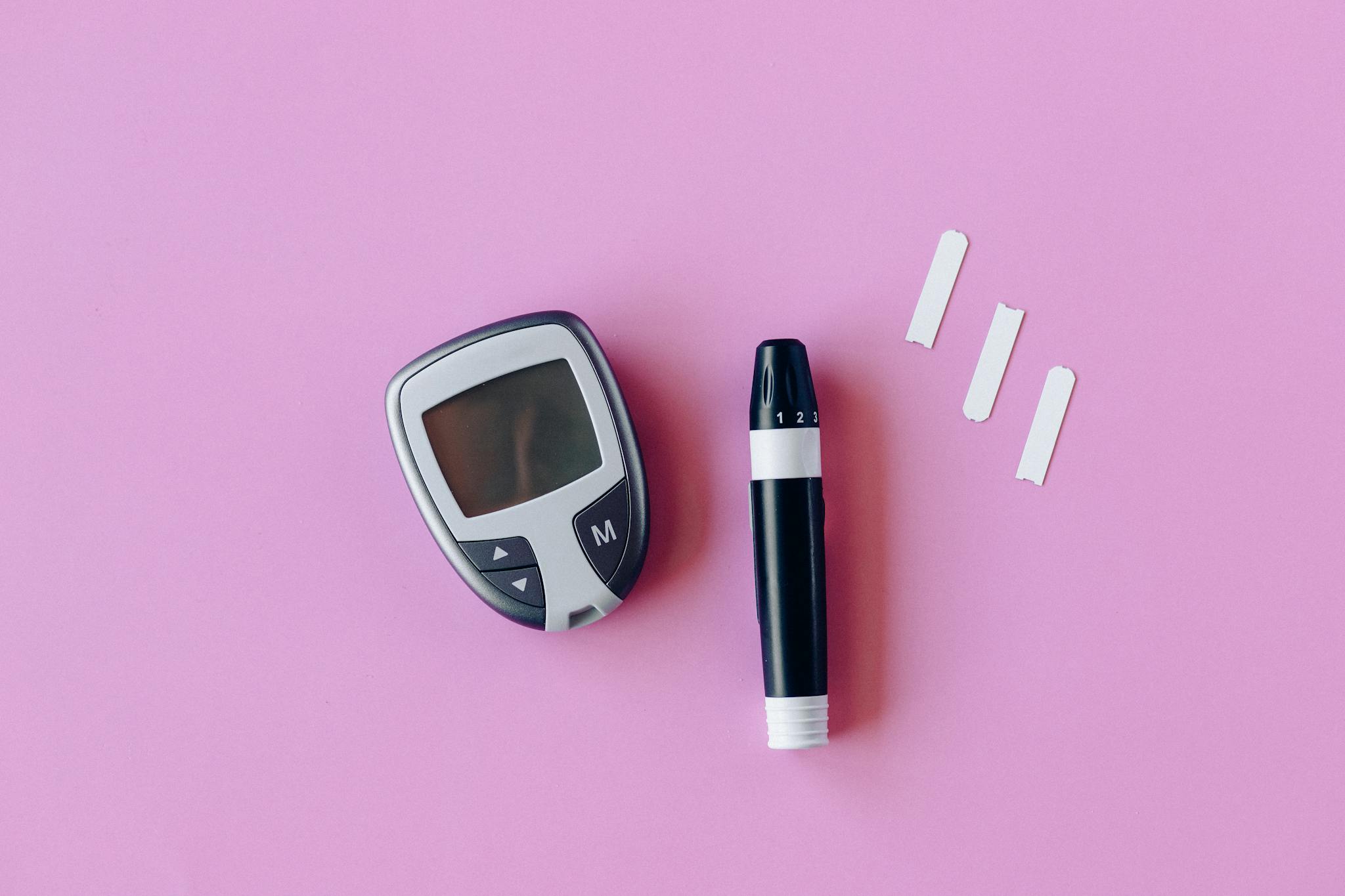 Flat lay of diabetes testing kit with glucometer and lancet on pink surface.