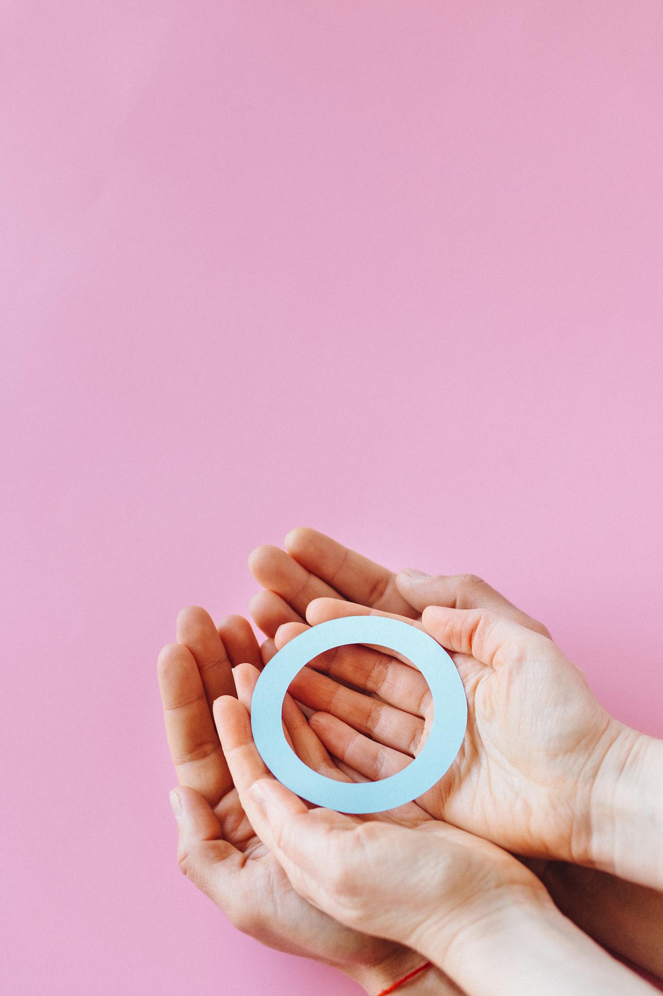 Two hands holding a blue circle symbolizing diabetes awareness against a pink background.